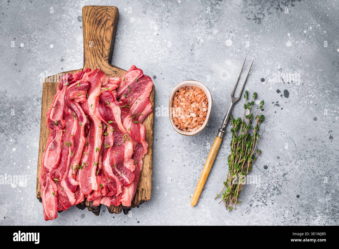 Lanières de viande de côtes courtes crues de qualité supérieure assaisonnées de sel et de thym, présentées sur une planche de bois Banque D'Images
