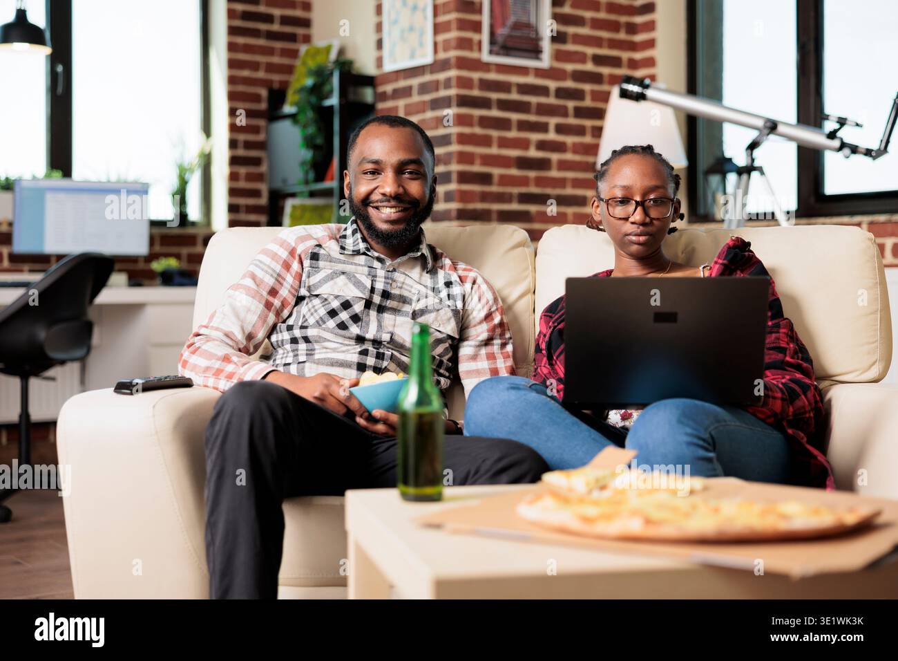 Portrait d'un homme regardant la télévision et d'une femme utilisant un ordinateur portable, naviguant sur Internet et s'amusant avec un film à la télévision. Repas de restauration rapide à emporter et boissons de bière. Banque D'Images