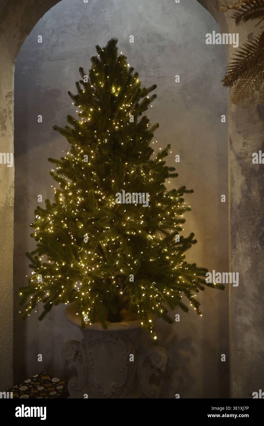 Sapin Evergreen avec une lumière jaune étincelante dans une pièce minimaliste. Concept de magie saisonnière, décoration élégante du nouvel an et atmo paisible du soir Banque D'Images