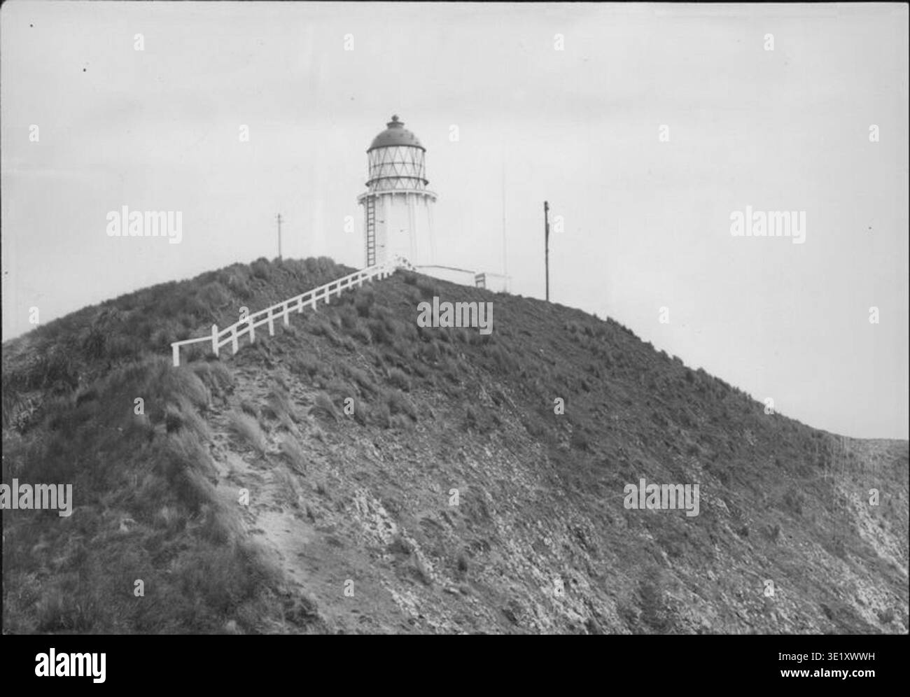 Le phare de Cape Maria van Diemen est situé à la pointe nord de l'île du Nord de Nouvelle-Zélande. Cette photographie d’archive, prise lors de la croisière *Hinemoa* en 1902, offre une vue vers le sud du phare. L'image capture l'environnement côtier accidenté et la navigation maritime essentiels à l'histoire des phares de Nouvelle-Zélande. Banque D'Images