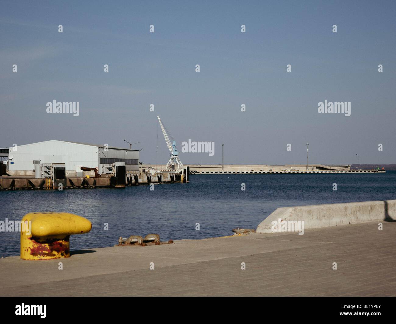 Borne d'amarrage jaune au bord du quai avec grue et entrepôt au port de Tallinn, Estonie, au début du printemps Banque D'Images