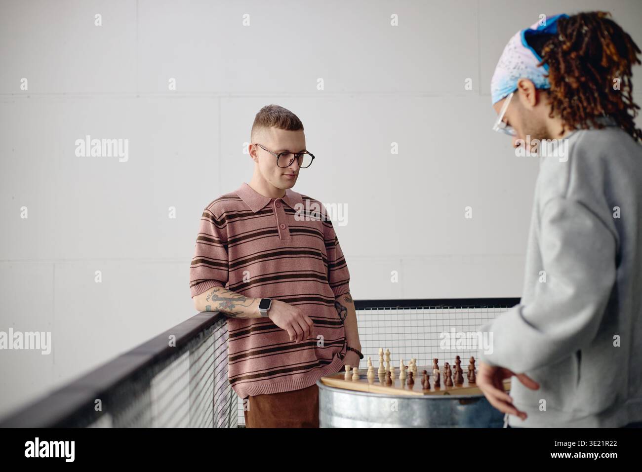 Jeune homme adulte jouant aux échecs avec un ami masculin biracial à l'intérieur Banque D'Images