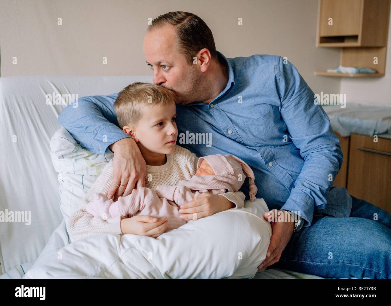 Père embrassant son fils aîné tout en tenant la petite fille nouveau-né. Moment familial émotionnel montrant l'amour et le lien entre les frères et sœurs. Banque D'Images