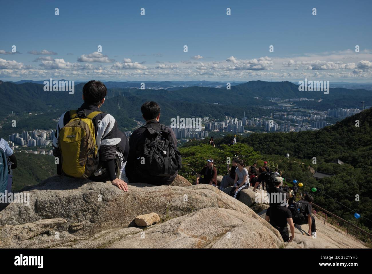 Séoul, Corée du Sud : deux jeunes hommes avec des sacs à dos assis sur des rochers au sommet de Gwanak Mountain bénéficiant d'une vue panoramique sur la ville de Séoul Banque D'Images