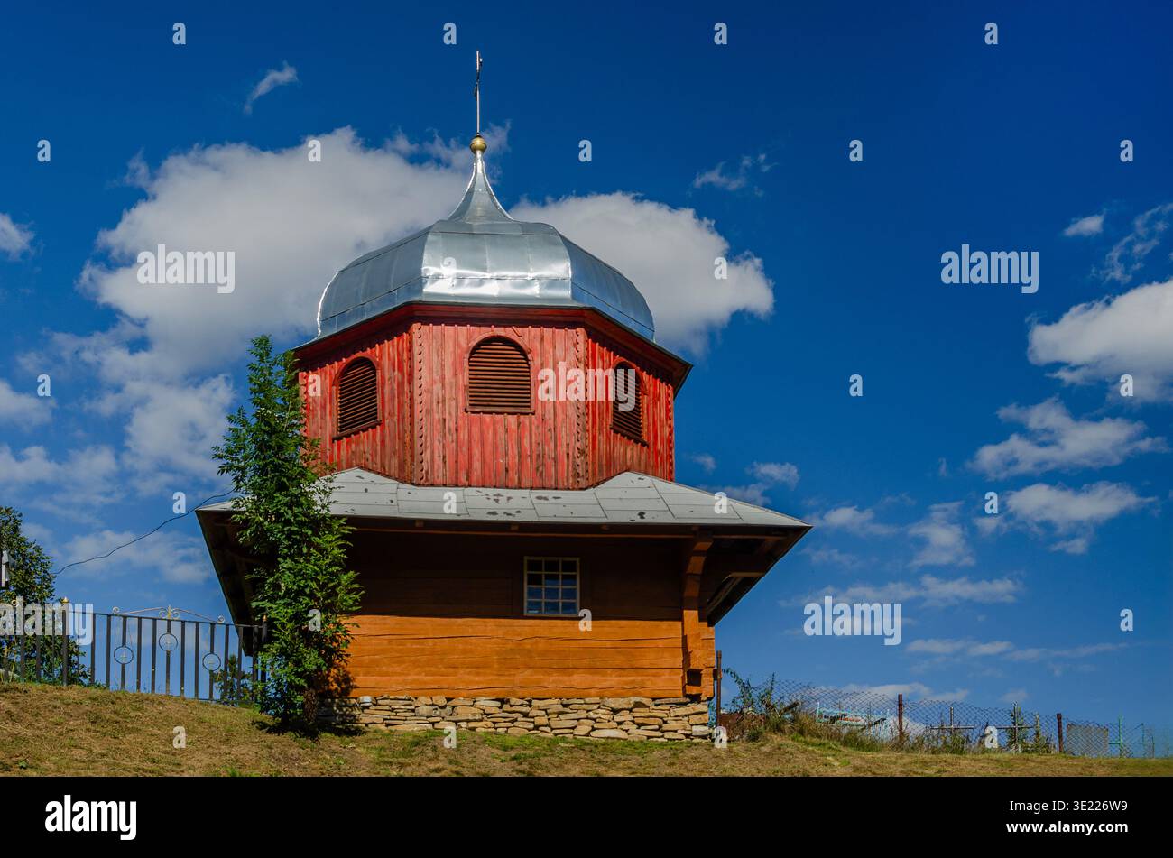 Une église hutsul en bois rouge éclatante dans les Carpates ukrainiennes présente un dôme en oignon argenté distinctif et un design octogonal, sur un bleu clair Banque D'Images