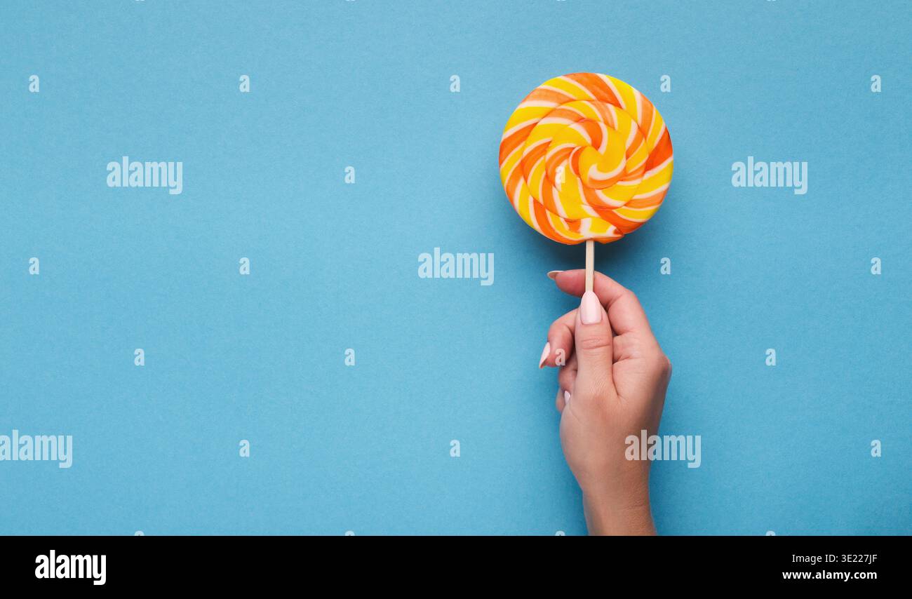 Sucette de bonbons en spirale dans la main sur fond bleu, vue de dessus Banque D'Images