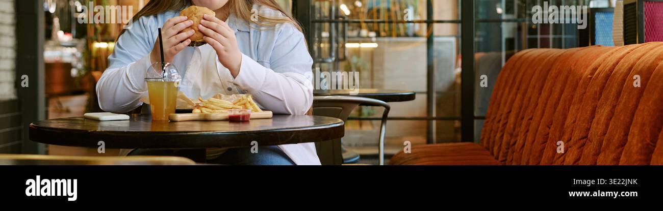 Jeune femme mangeant un hamburger et des frites à la table du restaurant Banque D'Images