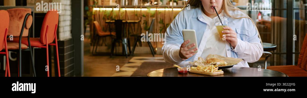 Jeune femme utilisant smartphone tout en buvant du jus et en mangeant Fast Food Banque D'Images