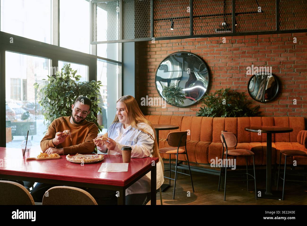 Jeune homme et femme partageant Pizza et riant dans Modern Cafe Banque D'Images