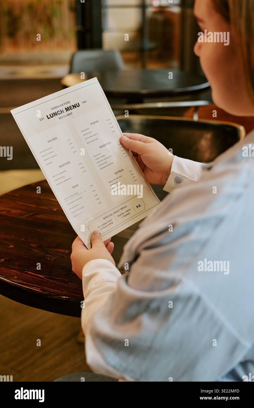 Jeune femme lisant le menu du déjeuner tout en étant assise à l'intérieur du restaurant Banque D'Images