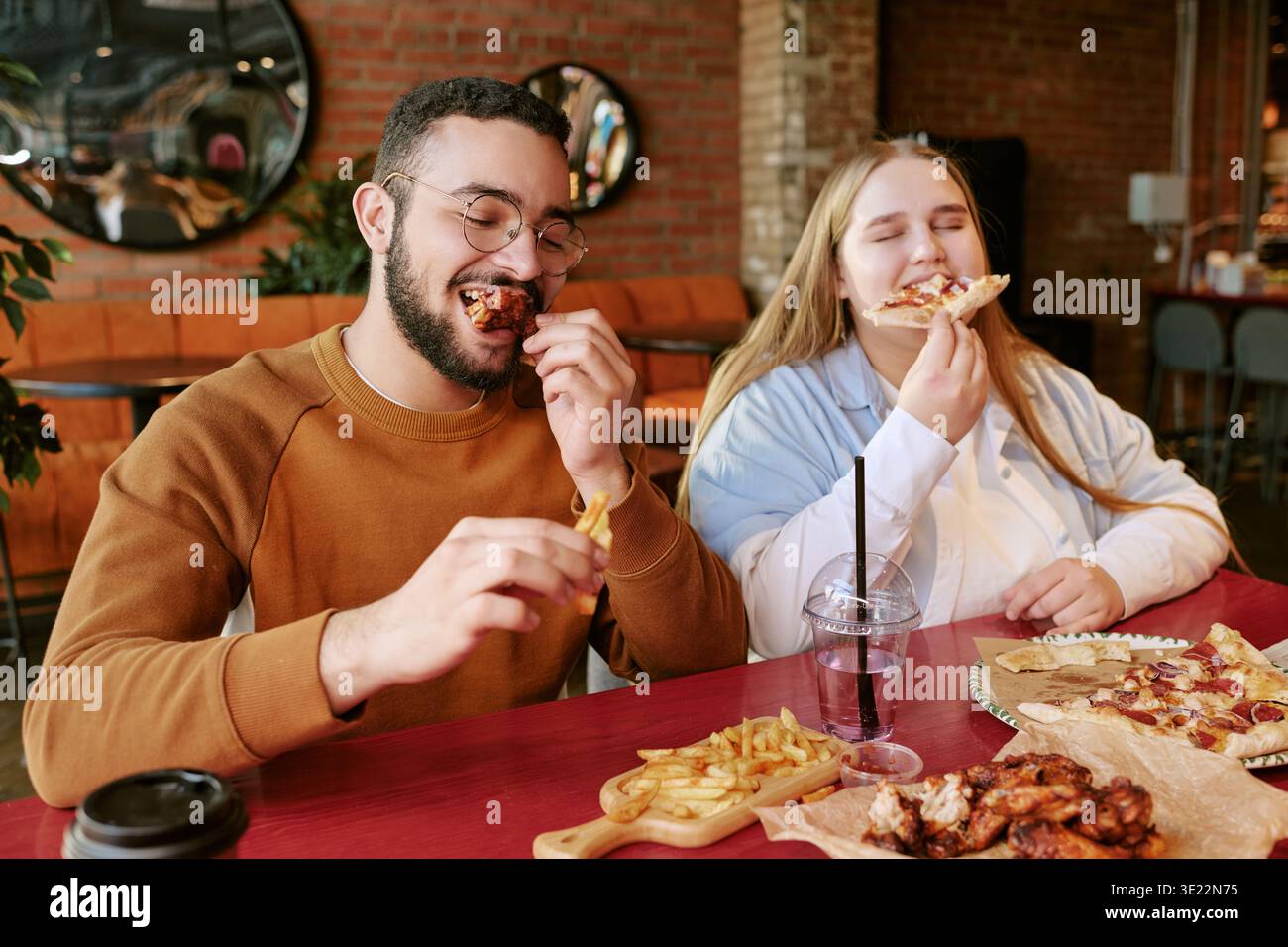 Jeune homme et femme appréciant manger Pizza et frites à l'intérieur Banque D'Images