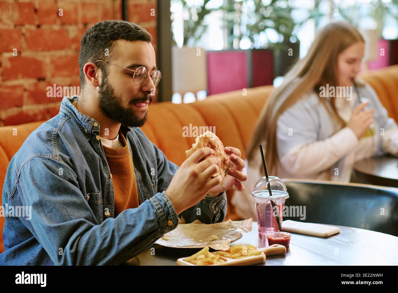 Jeune homme adulte appréciant de manger un hamburger et des frites au restaurant Banque D'Images