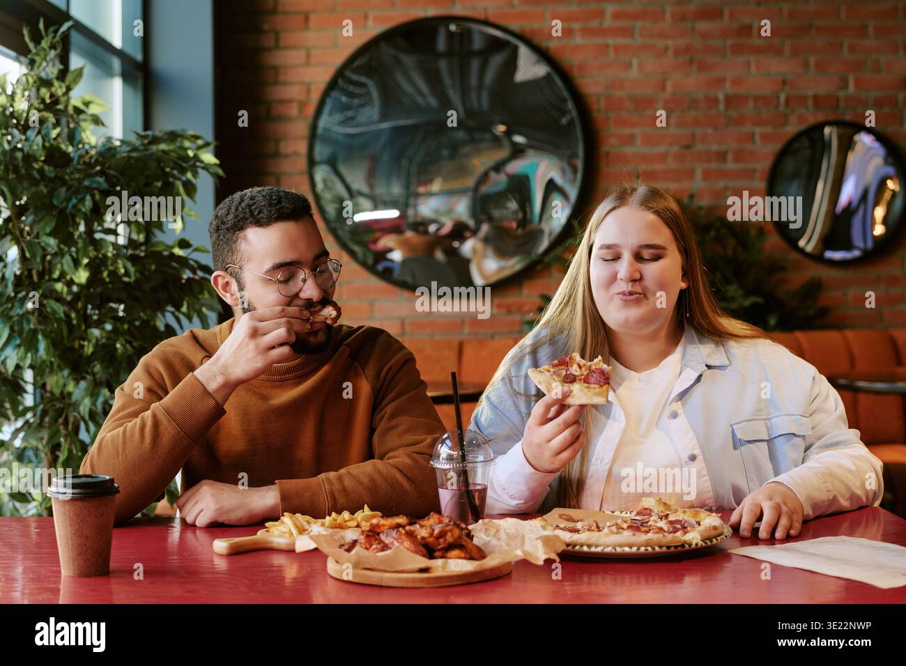 Jeune femme et jeune homme appréciant manger Pizza ensemble à l'intérieur Banque D'Images