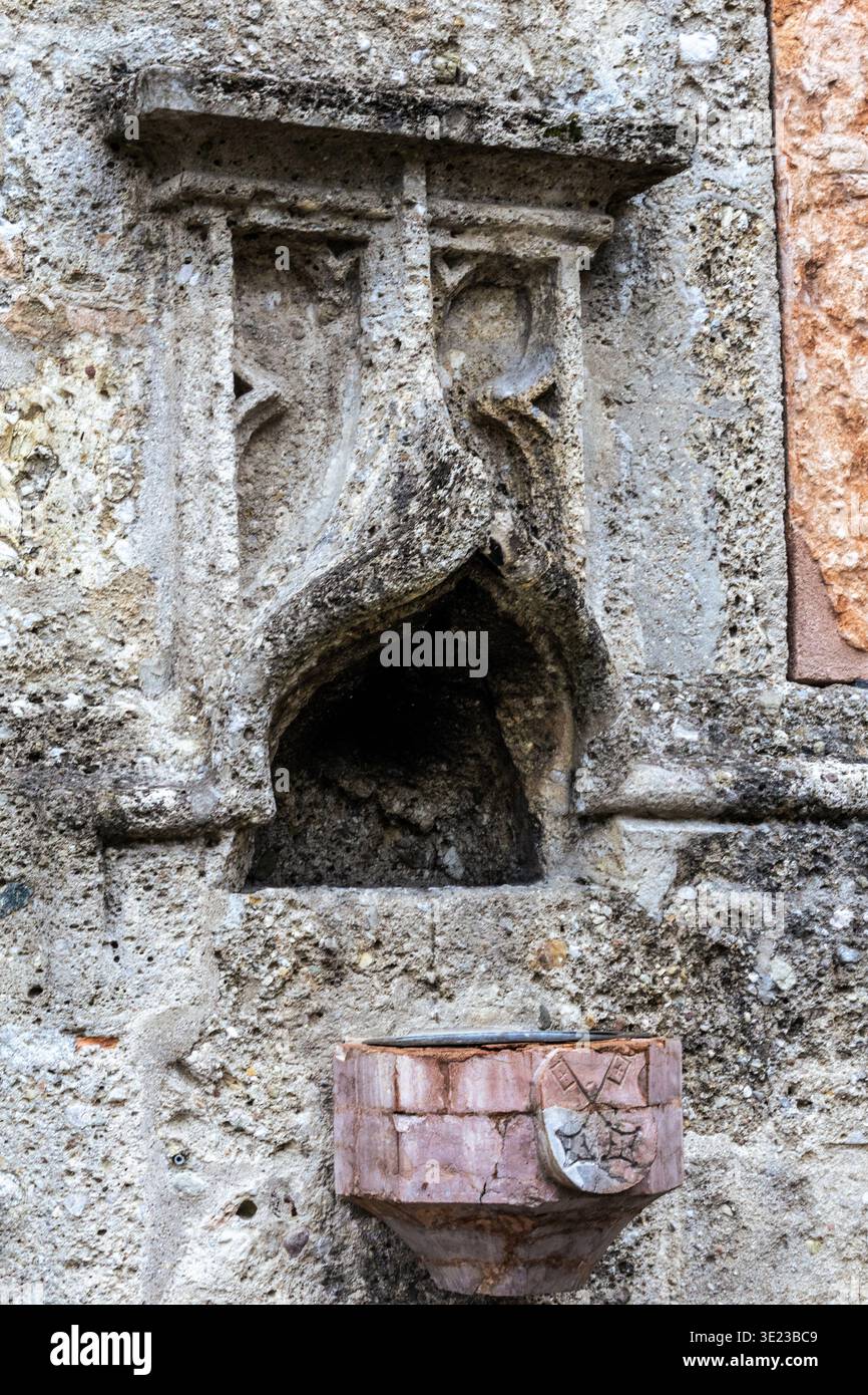 Gros plan d'une fontaine en pierre altérée attachée à un ancien mur de pierre. La fontaine dispose d'un bassin sculpté et d'un bec décoratif en pierre, sh Banque D'Images