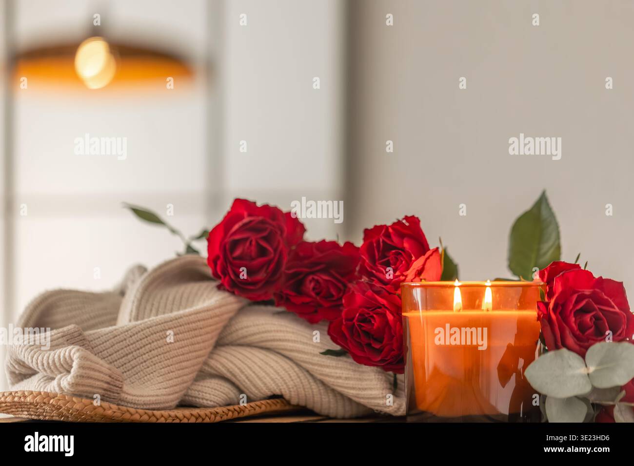 Bougie parmi les roses et couverture pour une ambiance de soirée maison. Lueur douillette. Banque D'Images