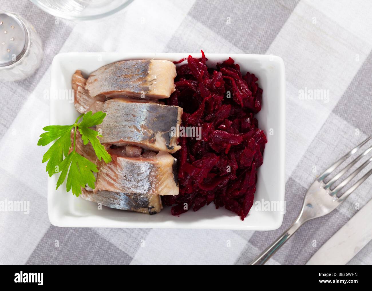 Salade de hareng appétissante avec betteraves, crème sure et persil dans une assiette blanche Banque D'Images