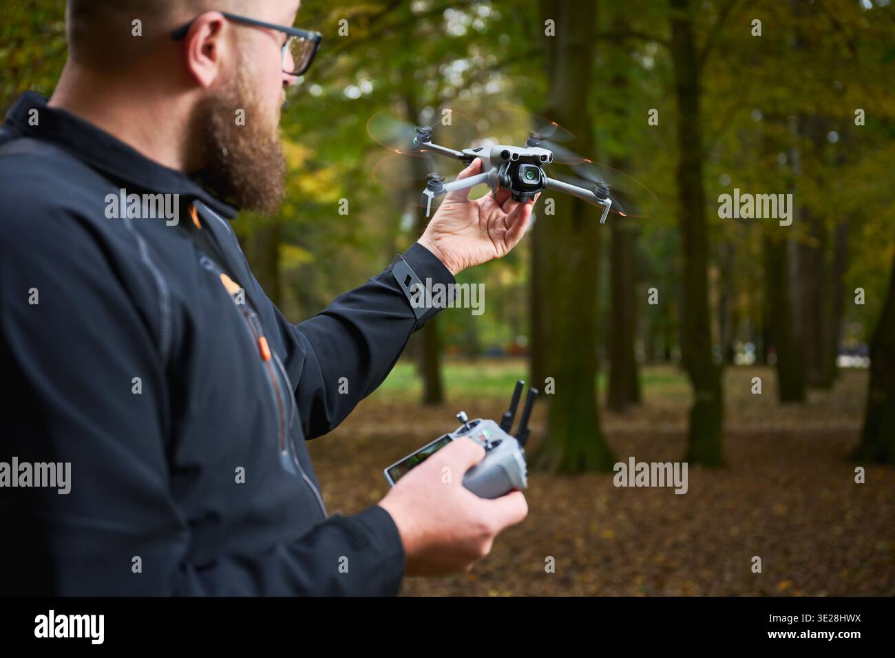 L'homme tient un drone volant et le contrôle avec la télécommande. Homme barbu opérant quadcopter dans un parc, testant le vol et surveillant les performances, concept de technologie moderne et passe-temps Banque D'Images