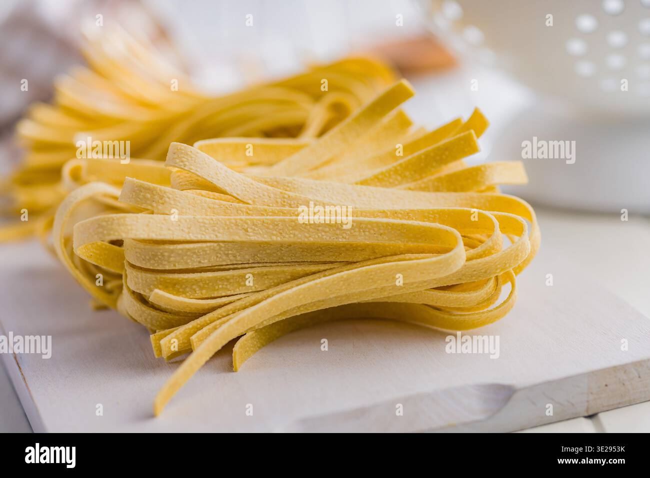 Les brins de pâtes fettuccine reposent sur une surface blanche, paraissant doux et frais. Ce type de pâtes est souvent utilisé dans divers plats. Banque D'Images
