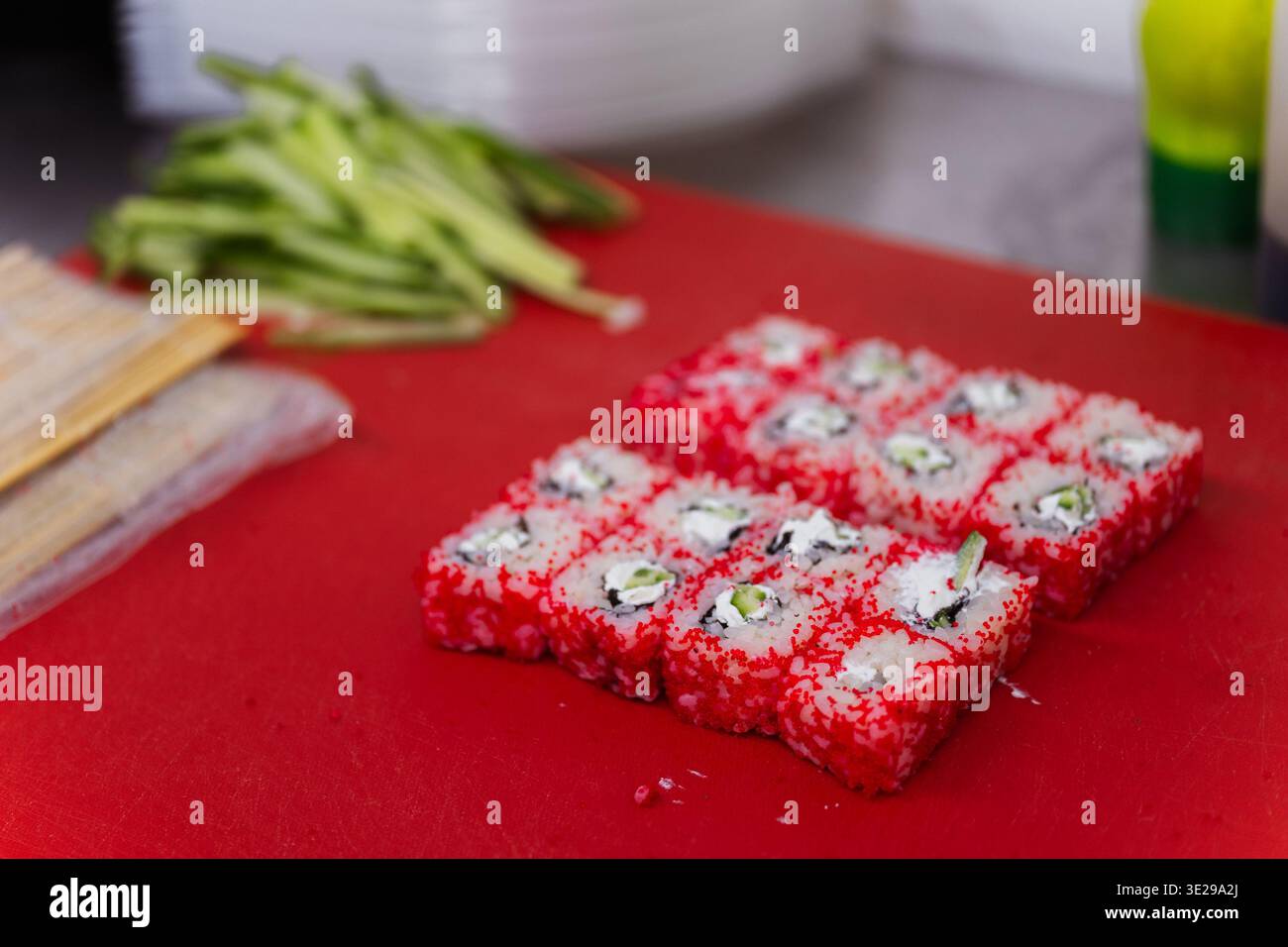 Rouleaux Tobiko rouge vif sur la planche à découper rouge à côté de l'avocat et du couteau, texture Roe brillant et soigné Banque D'Images