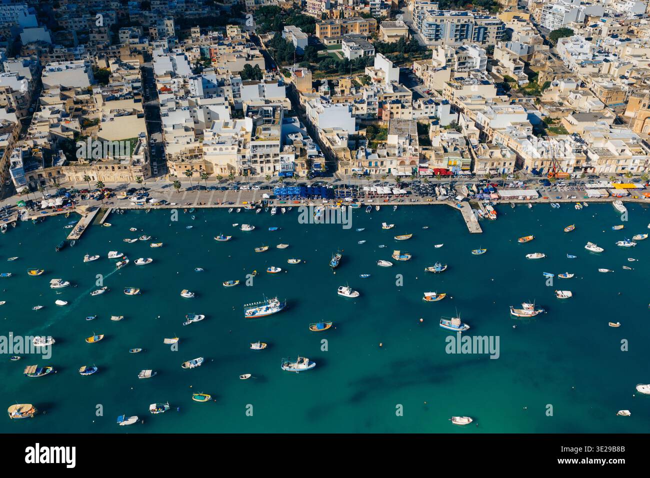 Vue aérienne du port tranquille parsemé de bateaux colorés contrastant avec les bâtiments anciens le long de la rive, Marsaxlokk, Malte. Banque D'Images