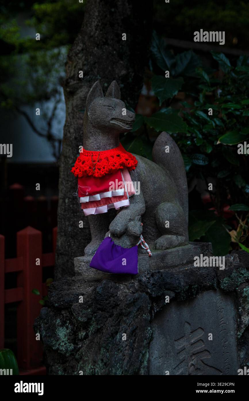Statue de renard en pierre avec bavoir rouge et sac violet au jardin du sanctuaire japonais, gardien spirituel Banque D'Images