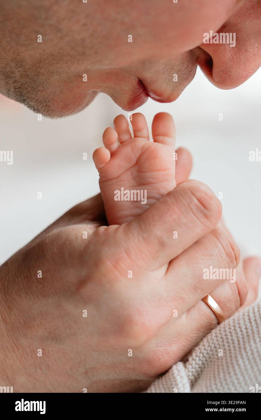 Père embrassant doucement les petits pieds de bébé nouveau-né. Moment de liaison émotionnelle exprimant l'amour, les soins et la connexion dans les premiers jours de la parentalité. Doux Banque D'Images