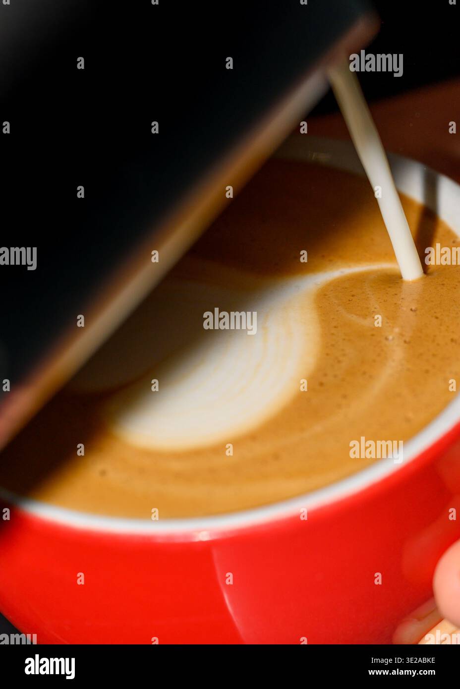 Gros plan du lait versé dans un espresso fraîchement préparé, créant des motifs de crème onctueux dans une tasse rouge, préparation de café macro Banque D'Images