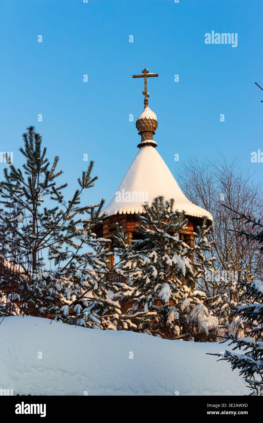 Flèche d'église orthodoxe en bois regardant à travers des branches de pin chargées de neige contre un ciel bleu clair d'hiver en Russie Banque D'Images