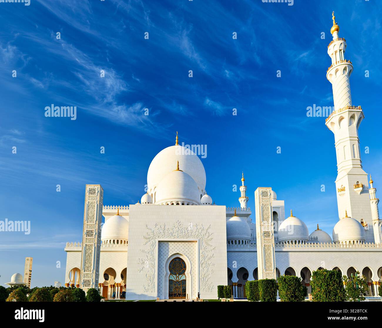Une mosquée à Abu Dhabi présente de grands dômes et un grand minaret contre un ciel bleu clair. Les gens visitent le site pour admirer son design. Banque D'Images