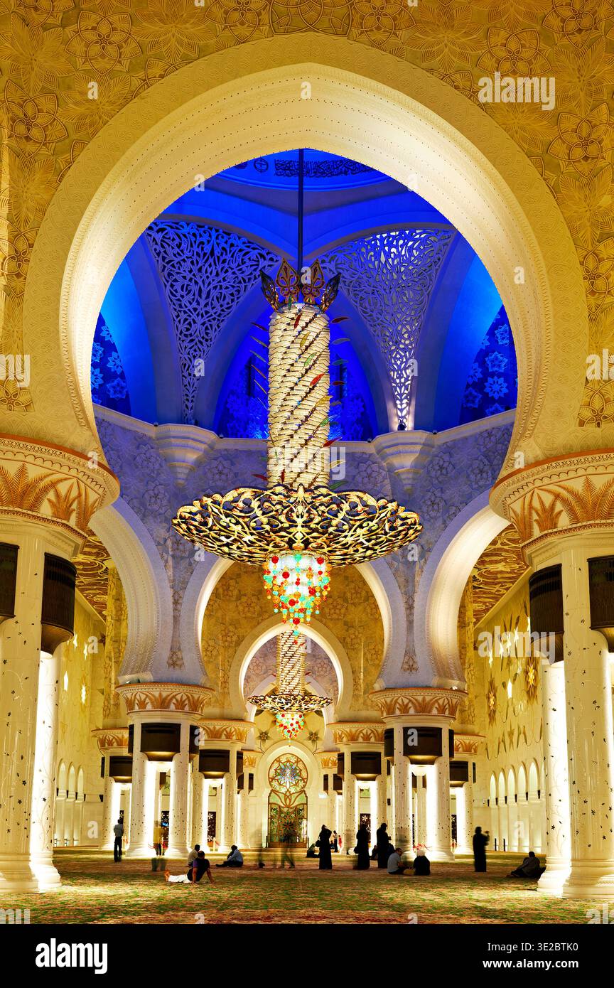 Les gens explorent l'intérieur de la Grande Mosquée Sheikh Zayed à Abu Dhabi. L'architecture présente de grandes arches et un éclairage élégant. Banque D'Images