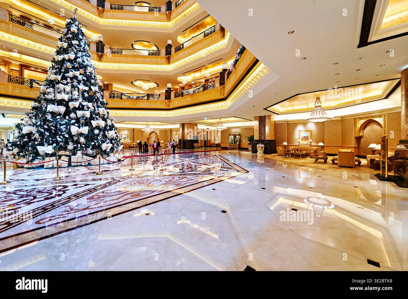 Les gens se promènent dans le hall de l'hôtel Abu Dhabi Emirates Palace. Un grand arbre de Noël est décoré au centre avec des lumières. Banque D'Images