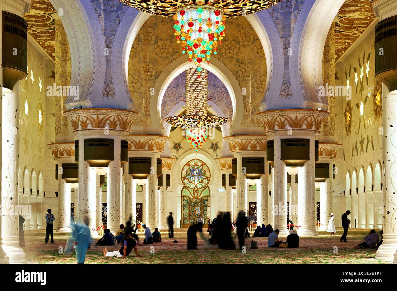 Les gens marchent et sont assis dans la Grande Mosquée Sheikh Zayed à Abu Dhabi. L'espace est bien éclairé avec des décorations ornées uniques. Banque D'Images