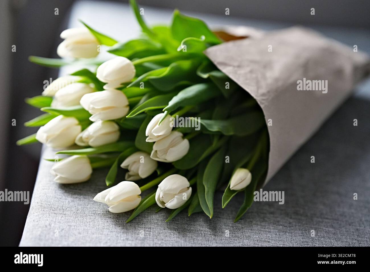 Un bouquet de tulipes blanches enveloppées dans du papier d'emballage simple repose sur la table. Photo horizontale Banque D'Images