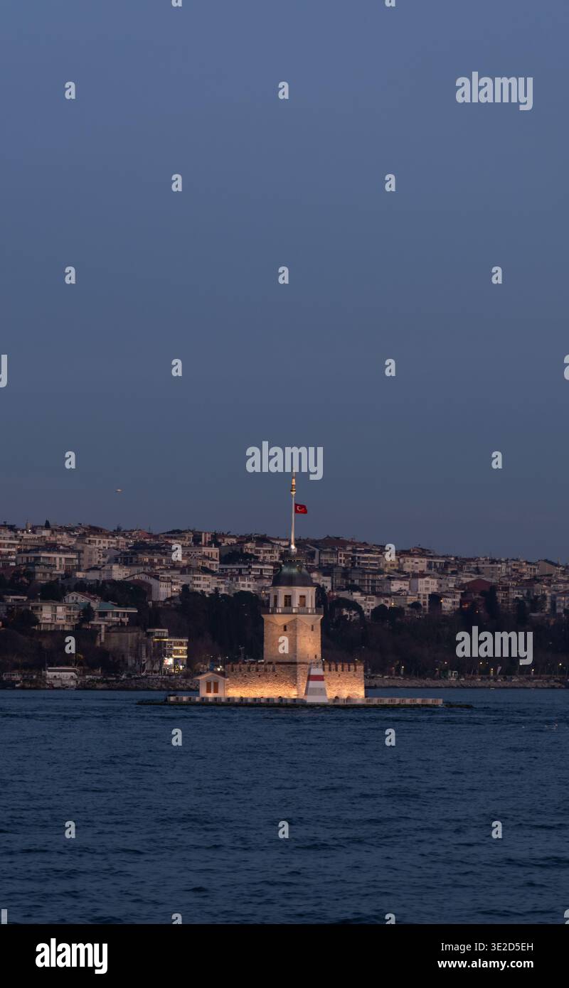 Vue au crépuscule de la Maiden Tower illuminée sur le Bosphore à Istanbul avec un drapeau turc et une colline dense gratte-ciel créant un voyage serein et lan Banque D'Images