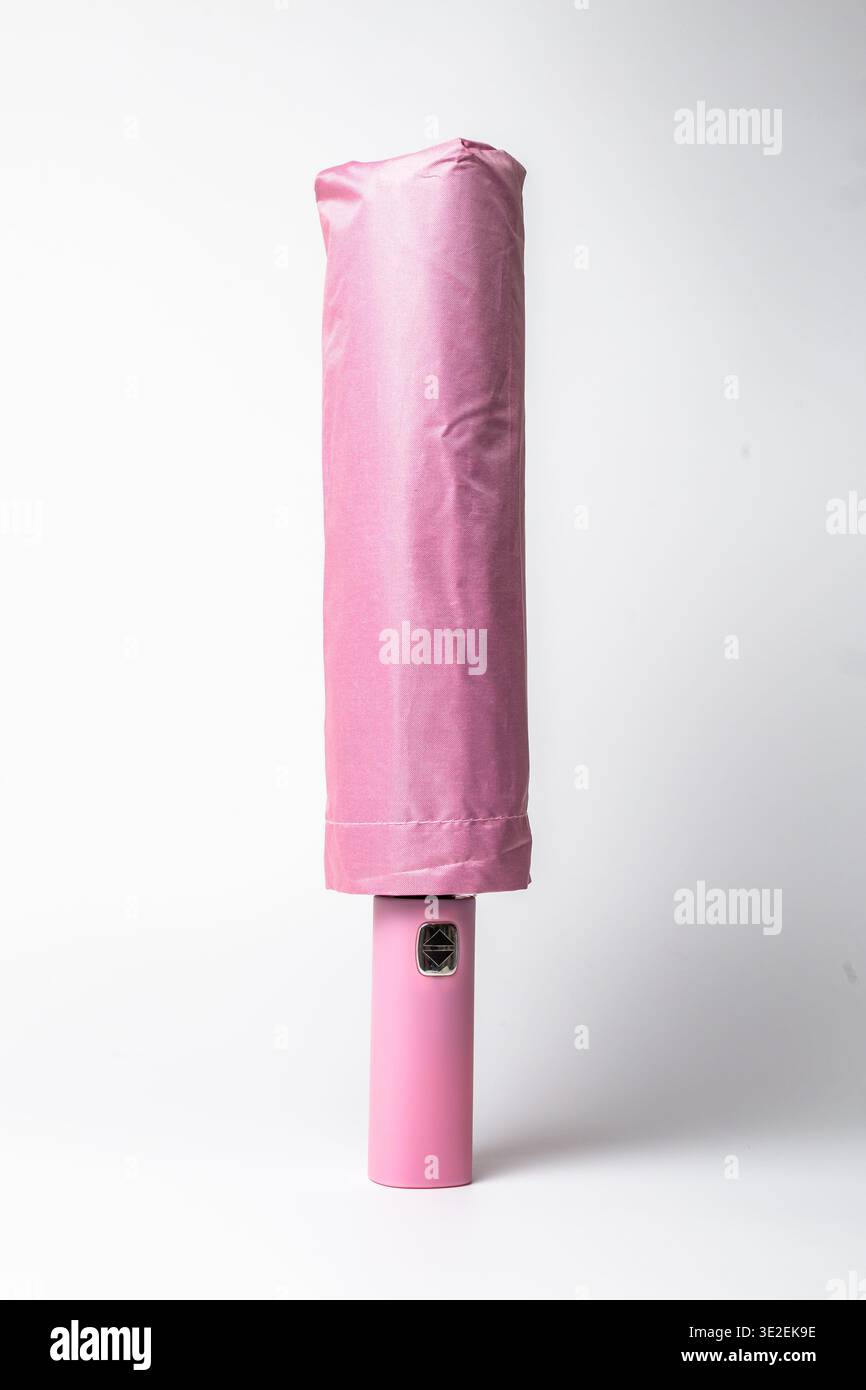 Élégant parapluie pliant compact en rose pastel doux, soigneusement enroulé et fixé avec une sangle, avec une pointe en métal brillant et un logo subtil. Banque D'Images