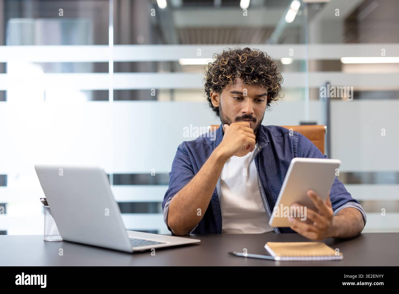 Portrait d'affaires d'un jeune homme indien travaillant sérieusement et soigneusement au bureau à l'aide d'une tablette. Banque D'Images