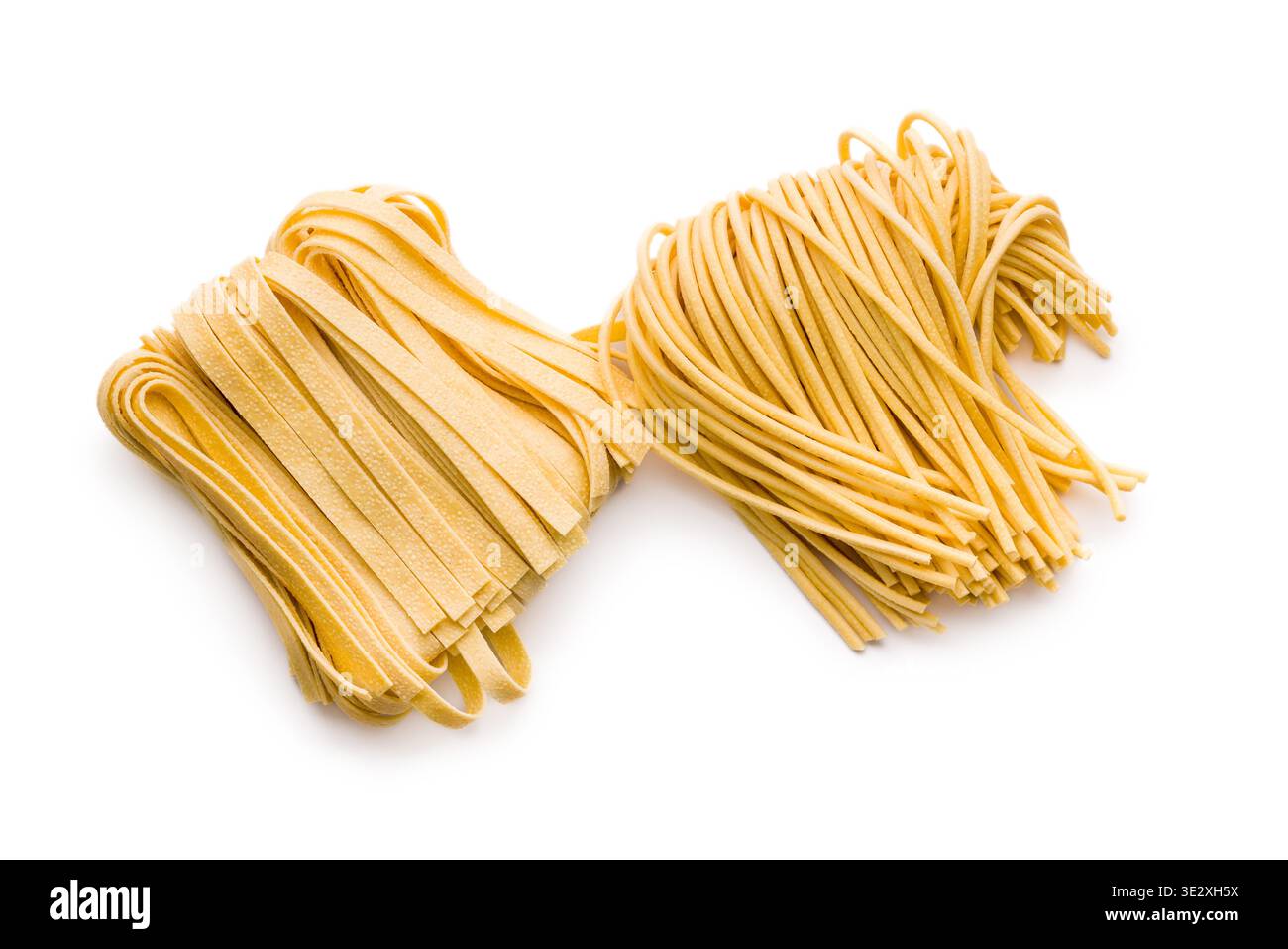Des brins de fettuccine et de bigoli reposent sur une surface blanche, paraissant doux et frais. Ce type de pâtes est souvent utilisé dans divers plats. Banque D'Images