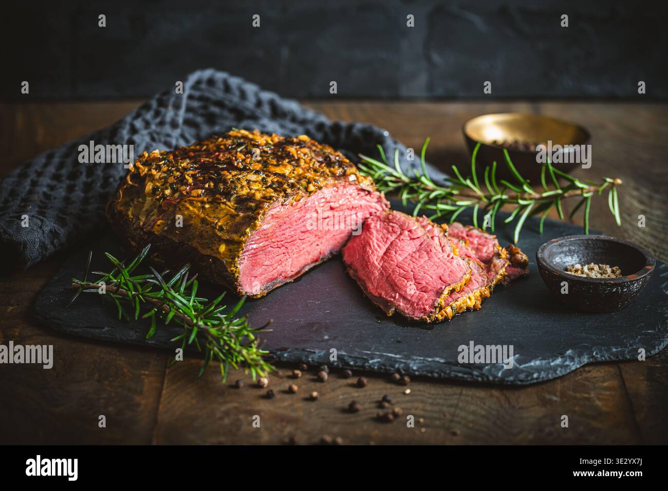 Rôti de boeuf avec une croûte de moutarde et d'herbes, frais du four, quelques tranches coupées ouvertes, sur une table en bois rustique Banque D'Images