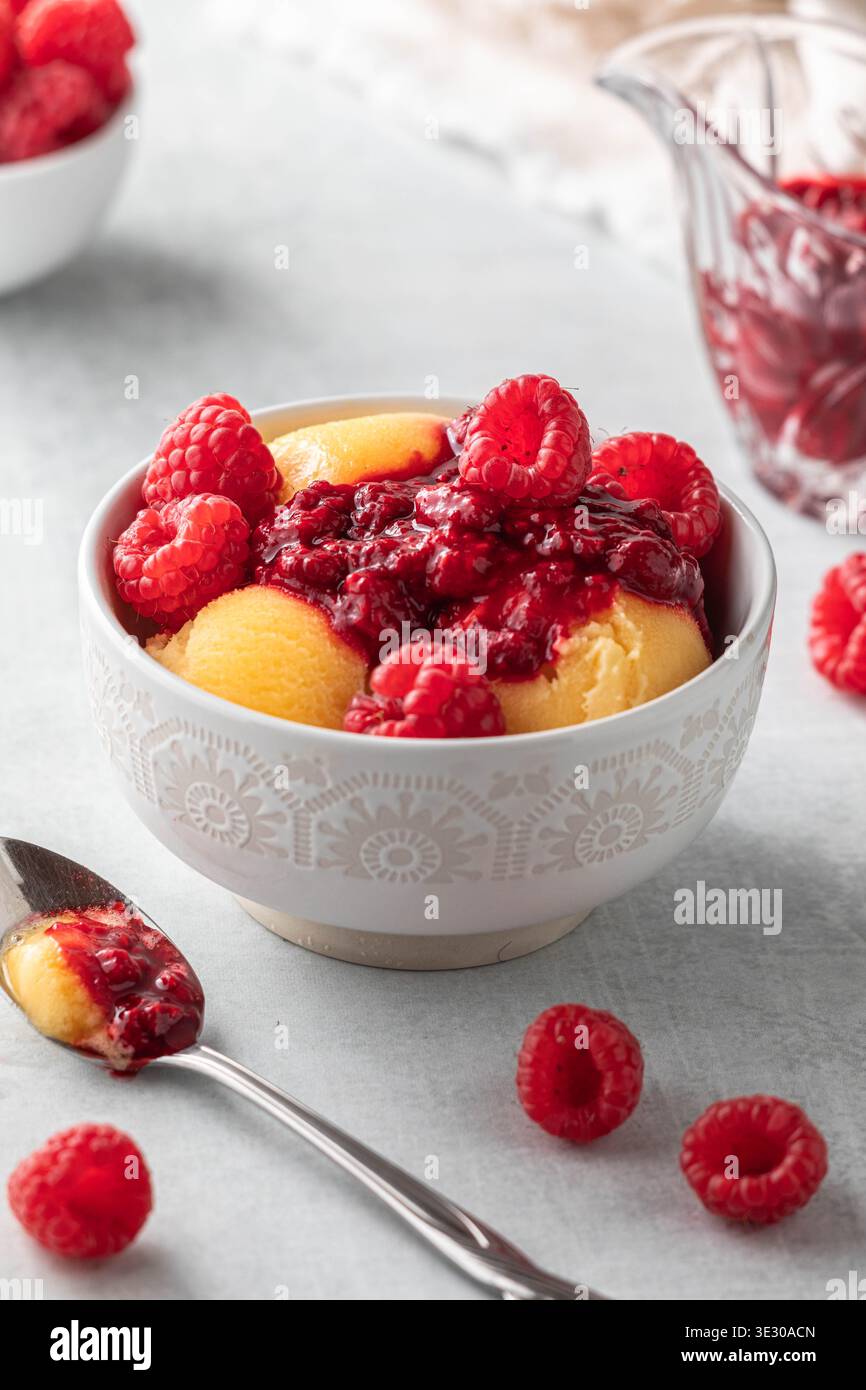 Sorbet à la mangue garni de coulis de framboises et de framboises fraîches. Banque D'Images