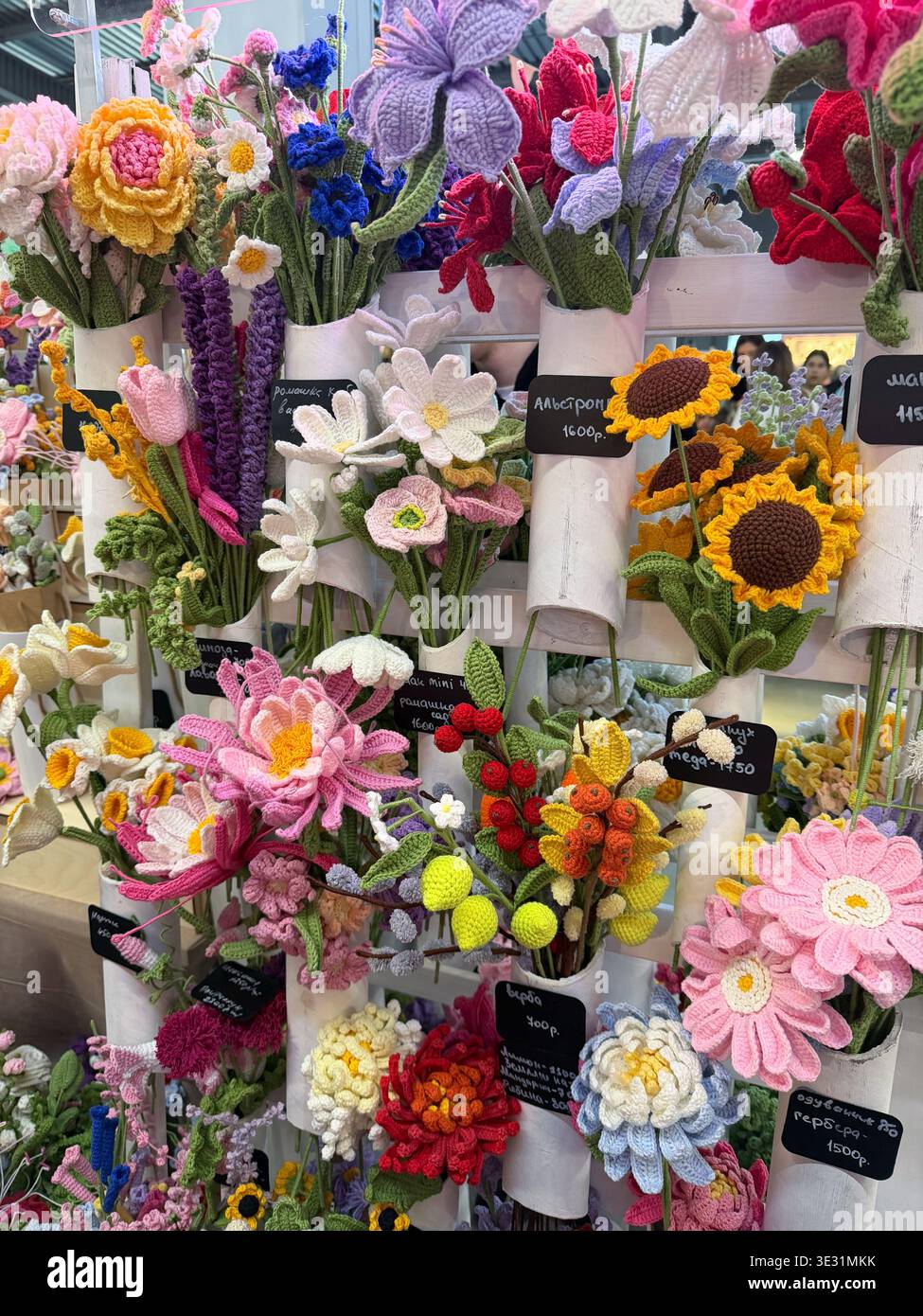 Moscou, Russie - 14 mars 2026 : fleurs tricotées faites à la main exposées dans des seaux à l'étal du marché avec des motifs colorés et des détails textiles dans la vente au détail Banque D'Images