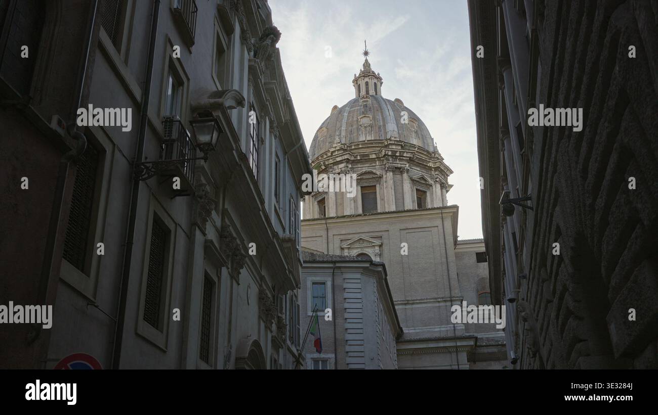 Dôme d'église en pierre au-dessus de la rue pavée étroite avec lanterne et drapeau italien accroché à la façade ; calme historique. Banque D'Images