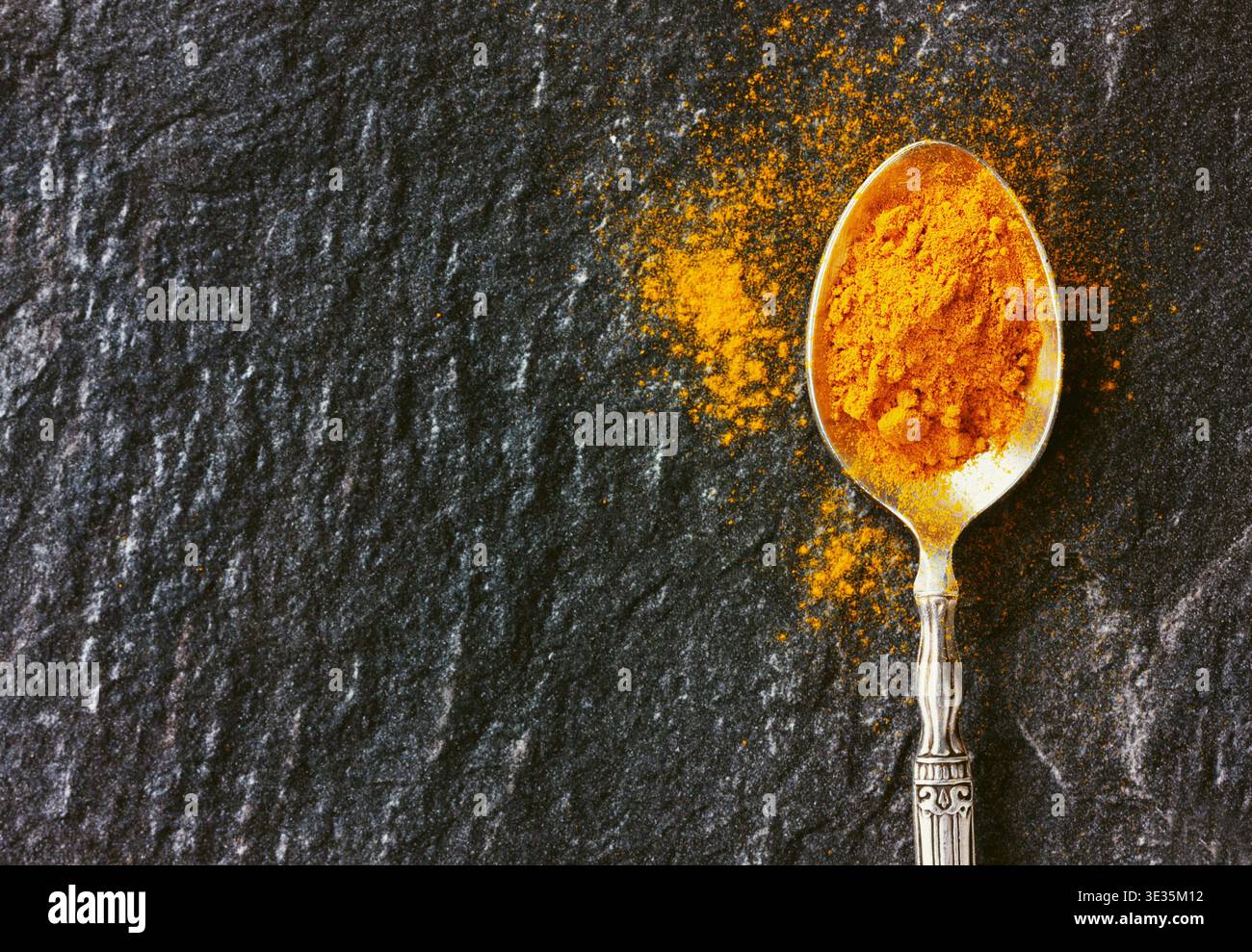 curcuma moulu en cuillère vintage argentée sur la surface de pierre noire Banque D'Images