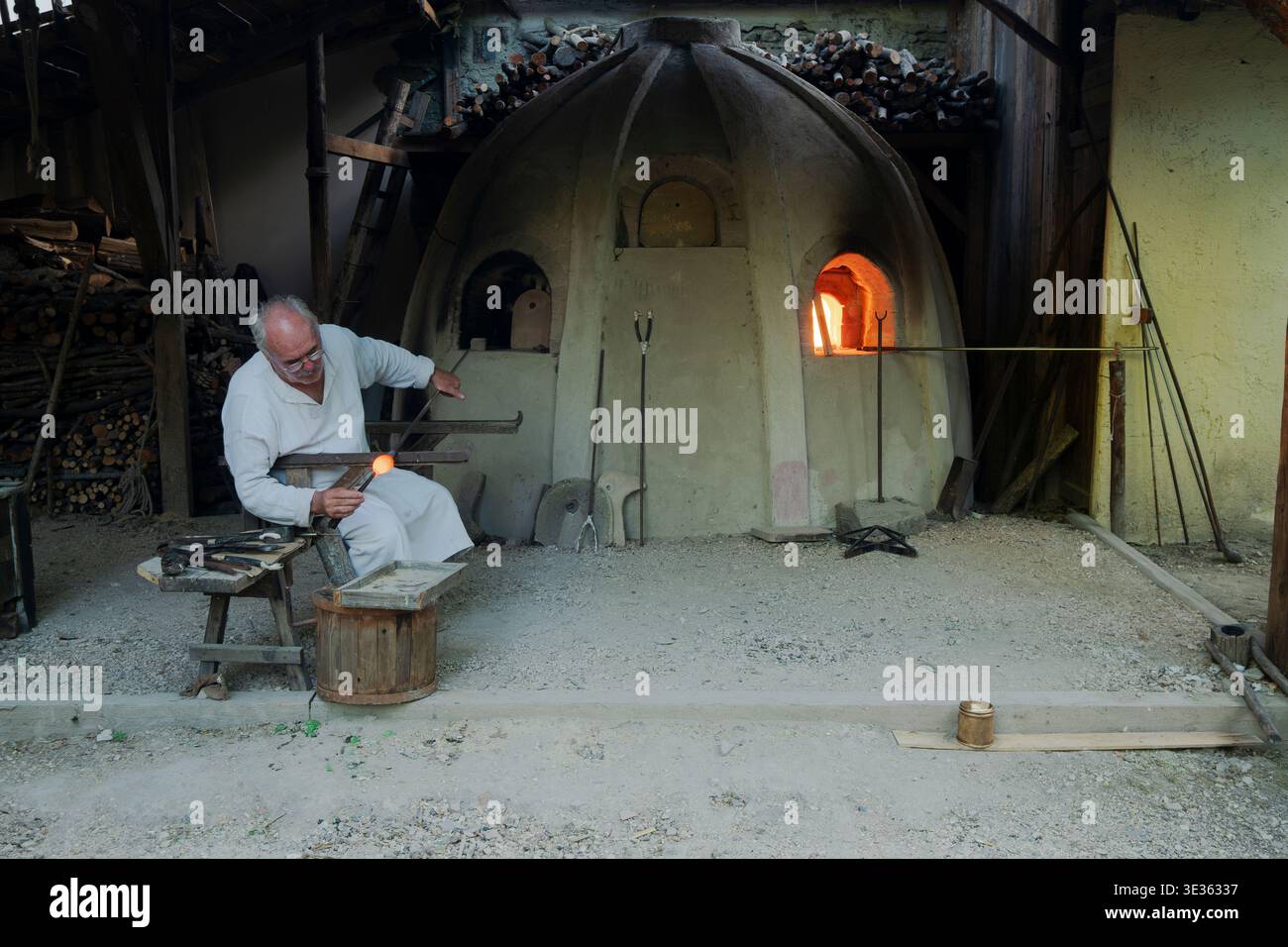 Artisan adulte mûr travaillant avec du verre fondu près d'un four traditionnel dans un ancien atelier, bevagna, Italie Banque D'Images