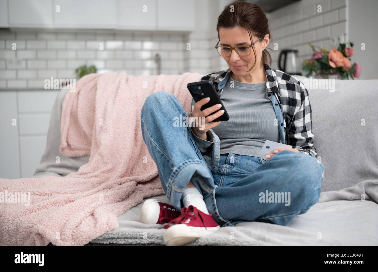 Jeune femme assise sur Sofa Shopping en ligne avec smartphone sur Internet Banque D'Images