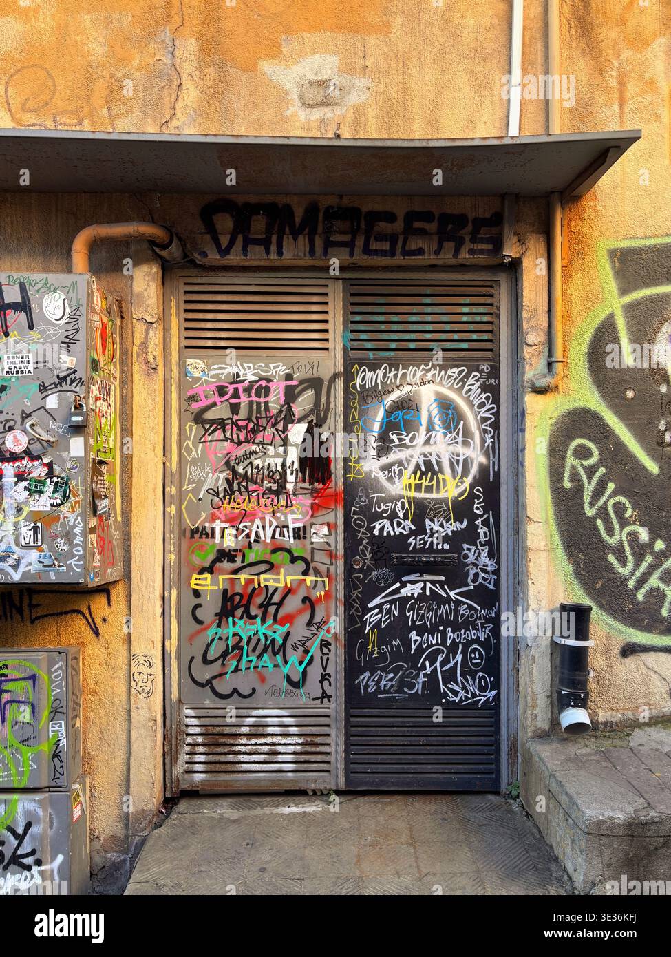 Porte en métal recouverte de graffitis près de la tour de Galata — art urbain de rue mêlant couleurs vives, symboles anarchistes et textures granuleuses dans Beyoğlu.10 mars 2026. Banque D'Images