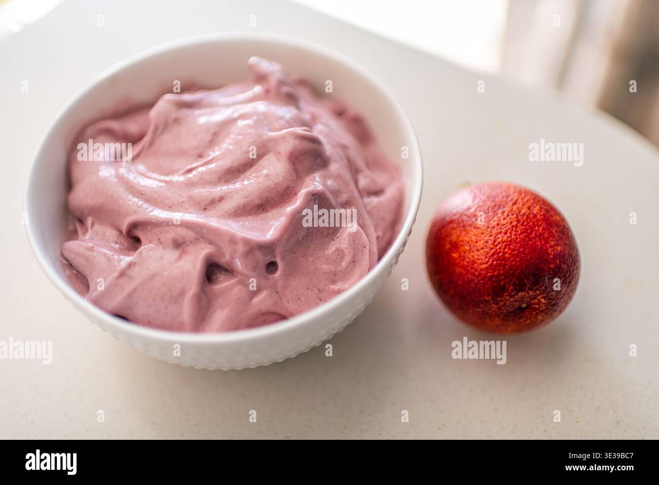 Assiette blanche colorée de crème glacée végétalienne à la banane mélangée avec des oranges sanguines avec des fruits de couleur rouge et violette Banque D'Images