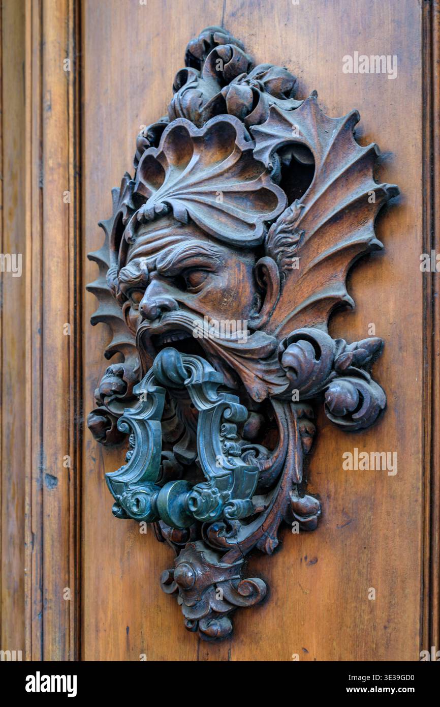 Frappeur de porte en métal de style Renaissance antique orné en forme de masque grotesque avec des ailes complexes sur une porte en bois altérée à Florence, en Italie Banque D'Images