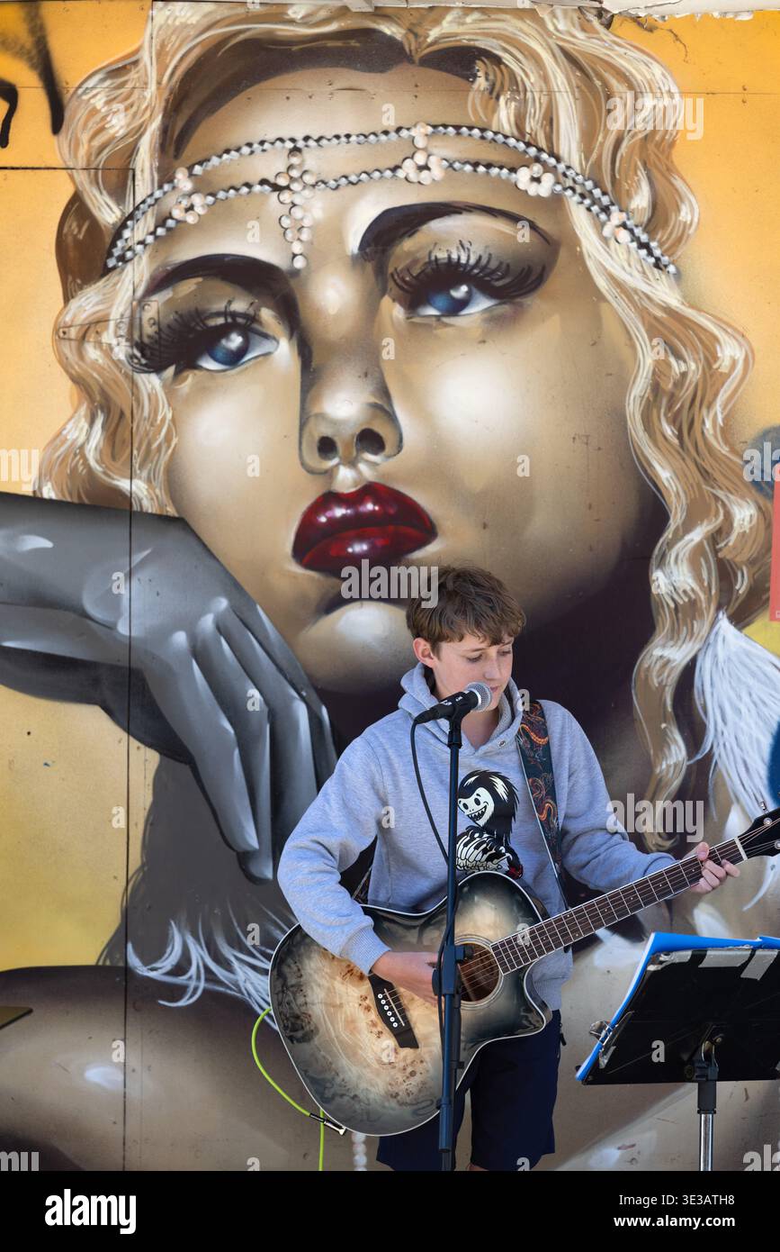 Jeune musicien de rue jouant de la guitare devant mural, Christchurch, Nouvelle-Zélande. Banque D'Images