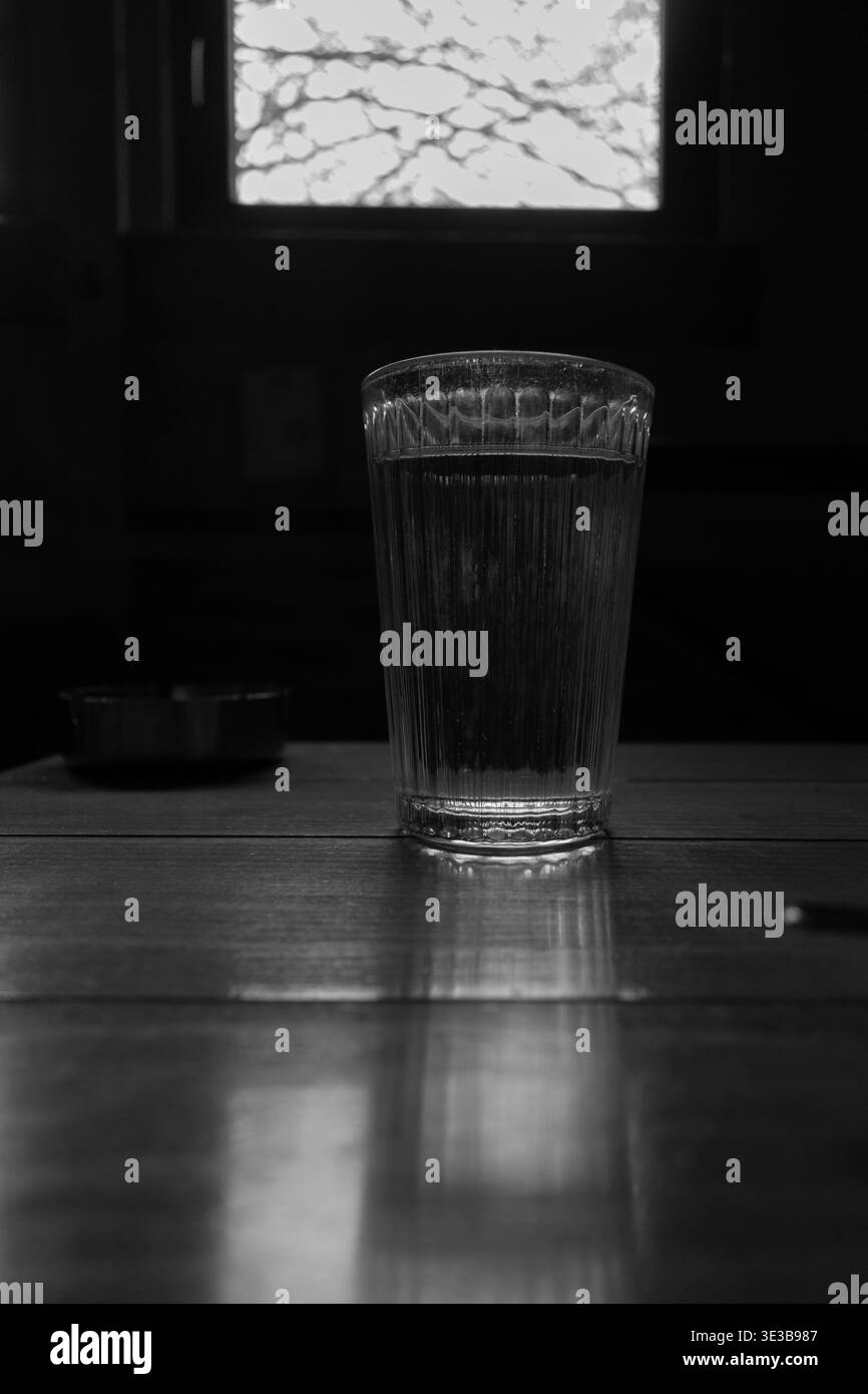 Un verre d'eau avec un reflet sur la table en bois et la lumière à travers la fenêtre. Banque D'Images
