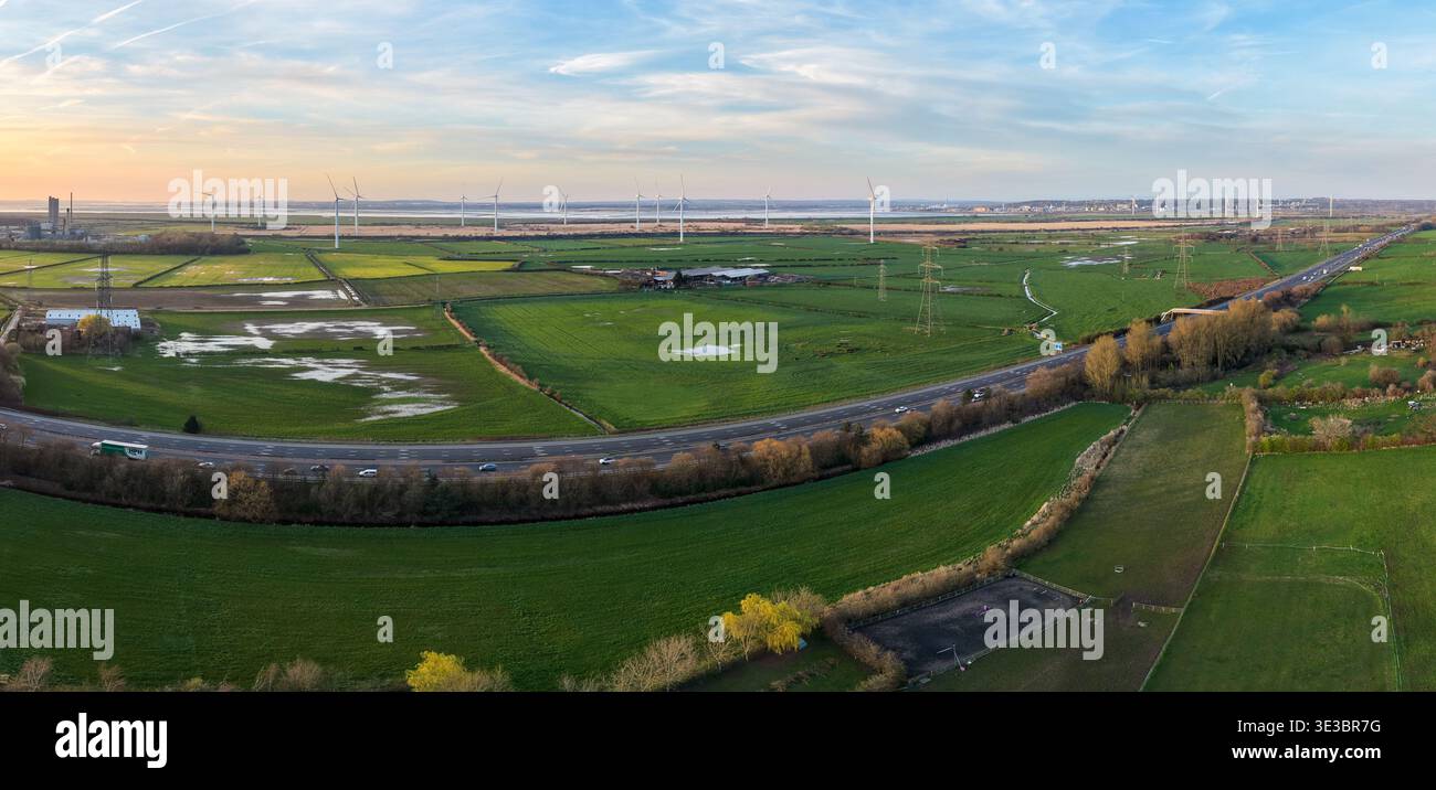 Une vue panoramique aérienne large de l'autoroute M56 qui courbe à travers la campagne du Cheshire au coucher du soleil, avec des parcs éoliens à énergie renouvelable. Banque D'Images